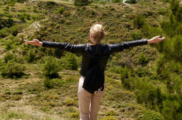 Nuori nainen seisoo kädet levitettyinä selkä kohti kameraa matalan vuoren päällä.