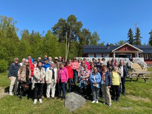 Vaasan ja Etelä-Pohjanmaan saaristoristeilylle osallistuneiden ryhmäkuva. Useampi kymmenen ihmistä poseeraa punaisen tuvan edessä ja katsoo kohti kameraa.