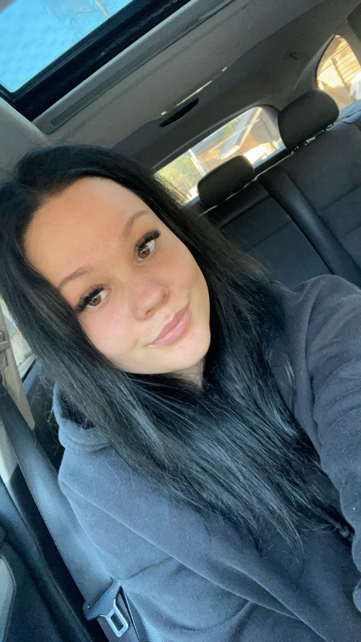 Nuori nainen katsoo autossa istuessaan kohti kameraa ja hymyilee. Kuva on selfie.