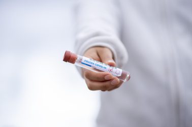 Henkilö pitelee käsissään koeputkea, jonka kyljessä lukee covid.