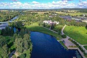 Maisema, jossa vesistön rannassa metsää, peltoa ja rakennuksia.